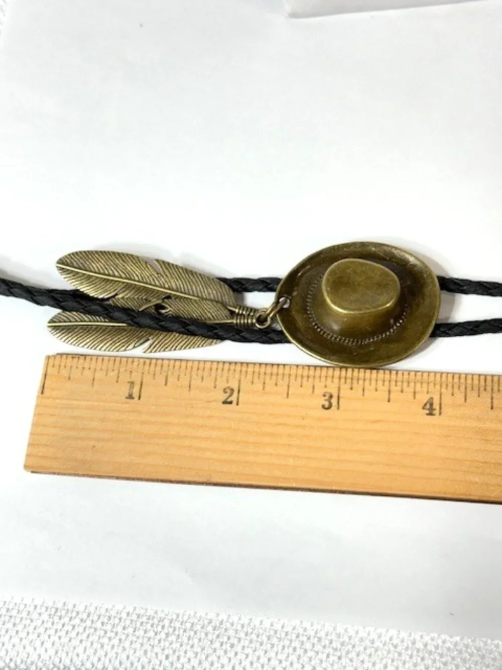 Gold-tone cowboy hat and feather, black cord western cowboy bolo tie.